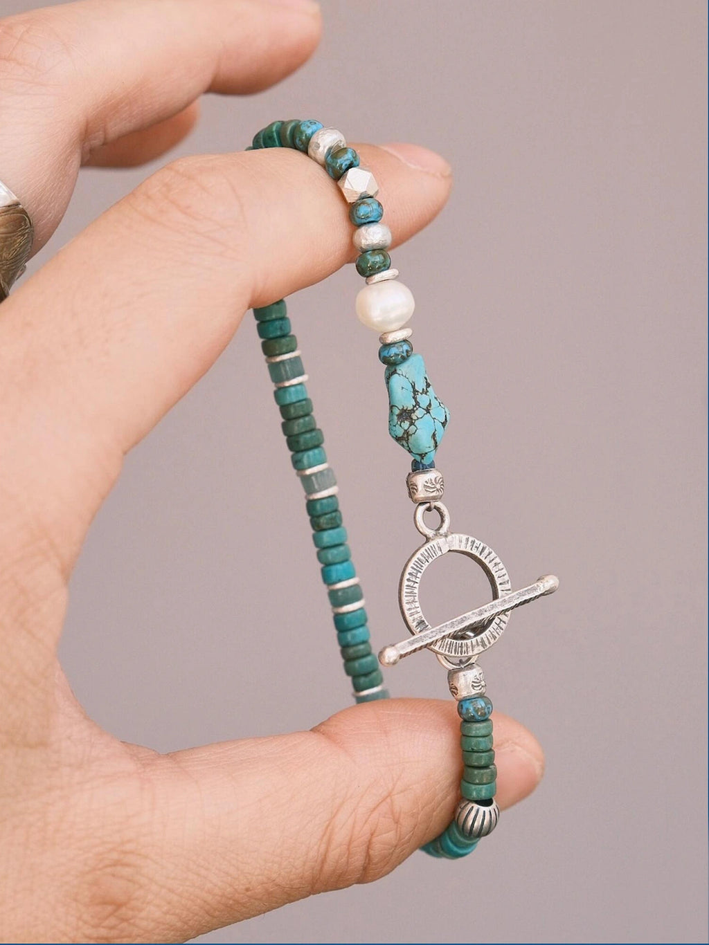 Hand holding Mineral Soul Series Mountain Tide bracelet, turquoise beads, baroque pearl and silver details in close-up view