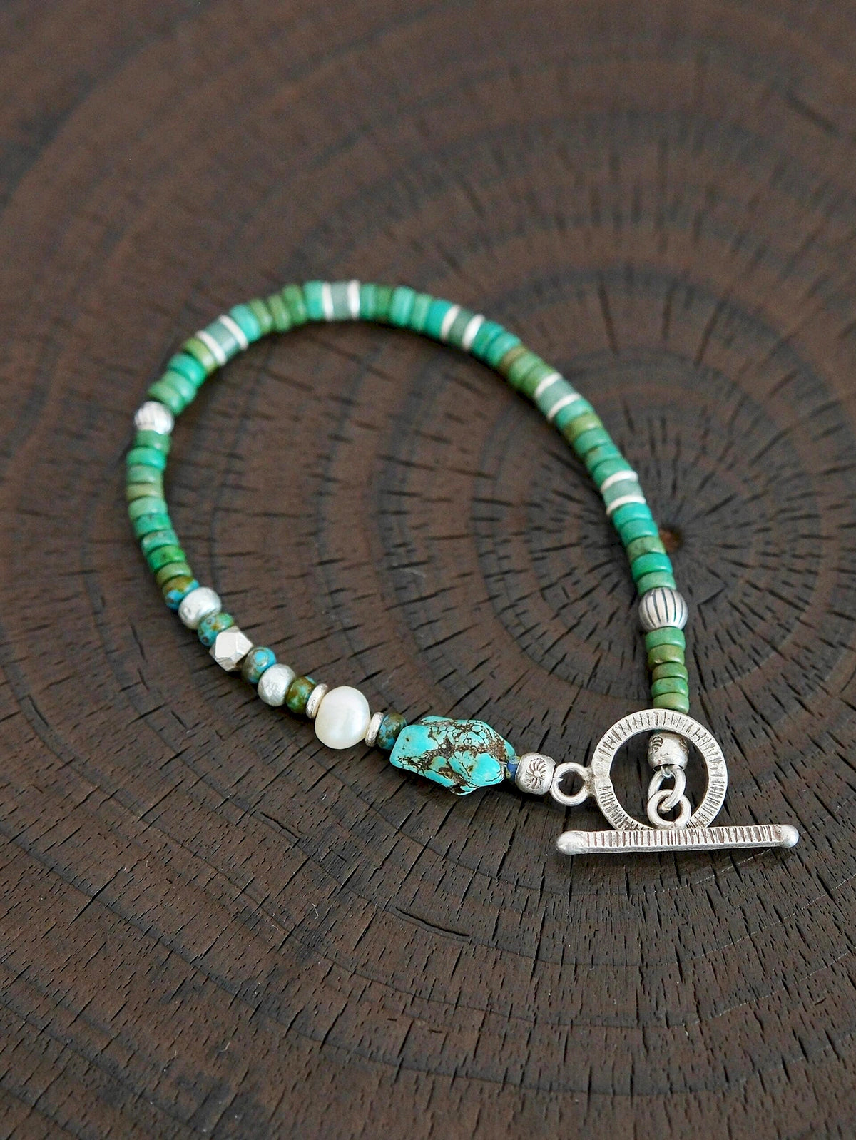 Flat lay of men’s turquoise, aventurine and pearl bracelet with hammered silver toggle clasp, natural mineral style
