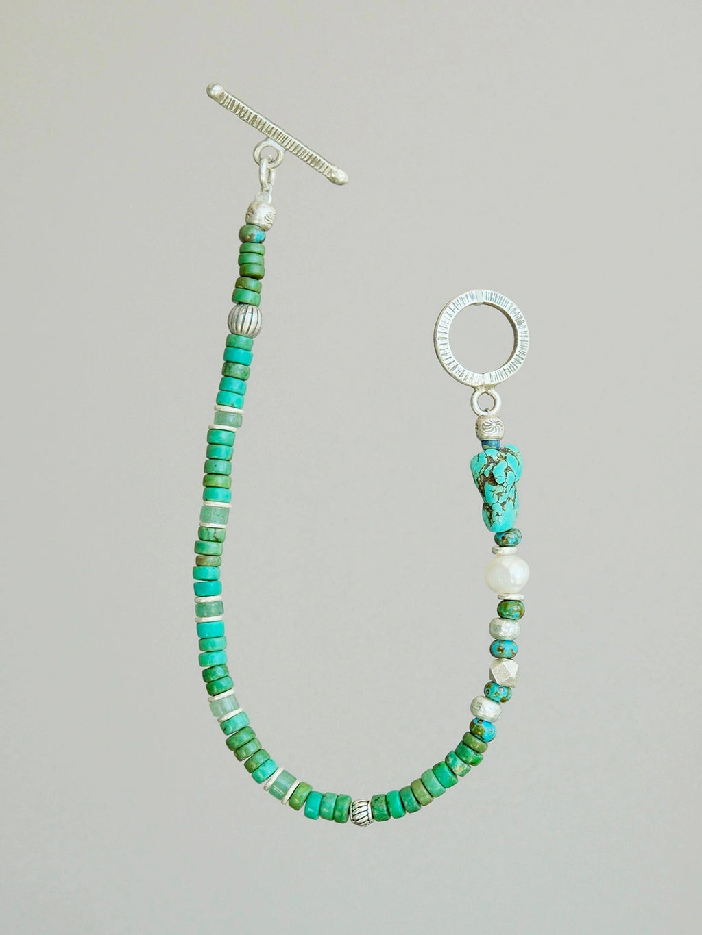 Flat lay of men’s turquoise, aventurine and pearl bracelet with hammered silver toggle clasp, natural mineral style