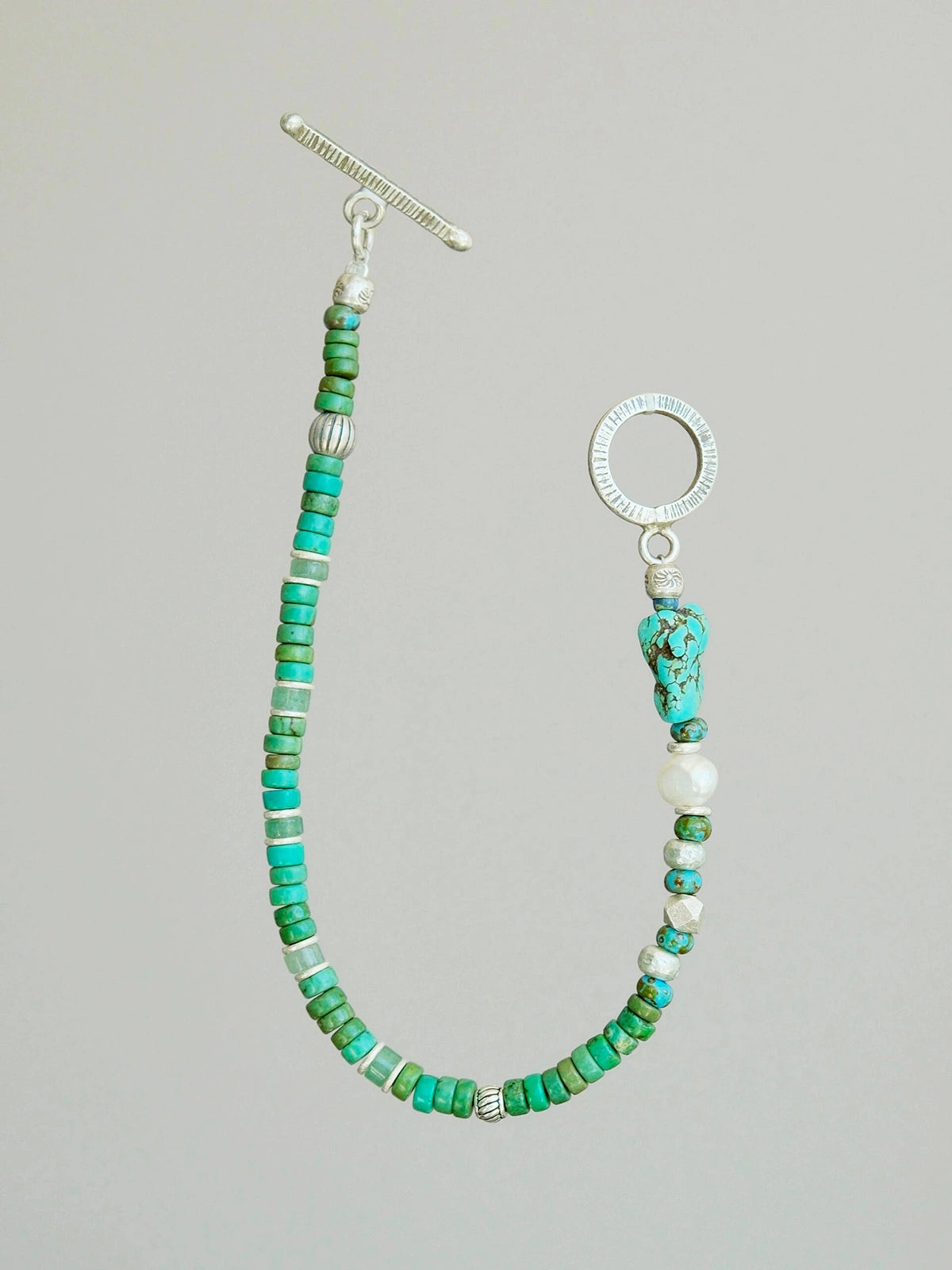 Flat lay of men’s turquoise, aventurine and pearl bracelet with hammered silver toggle clasp, natural mineral style