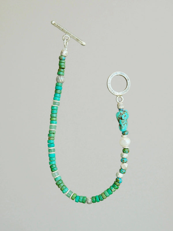 Flat lay of men’s turquoise, aventurine and pearl bracelet with hammered silver toggle clasp, natural mineral style