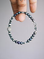 Handheld men’s pearl bracelet with hammered silver beads, close-up product view, Urban Stoic minimal style.