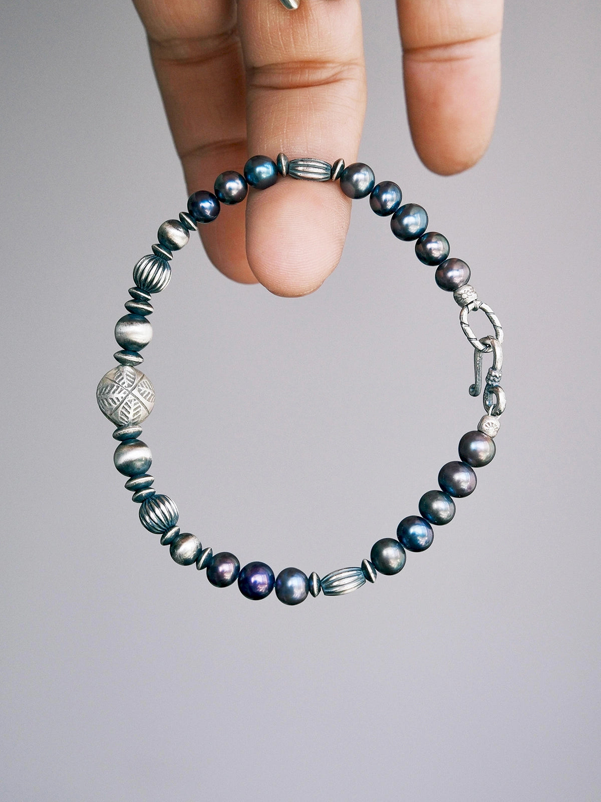 Handheld men’s pearl bracelet with hammered silver beads, close-up product view, Urban Stoic minimal style.