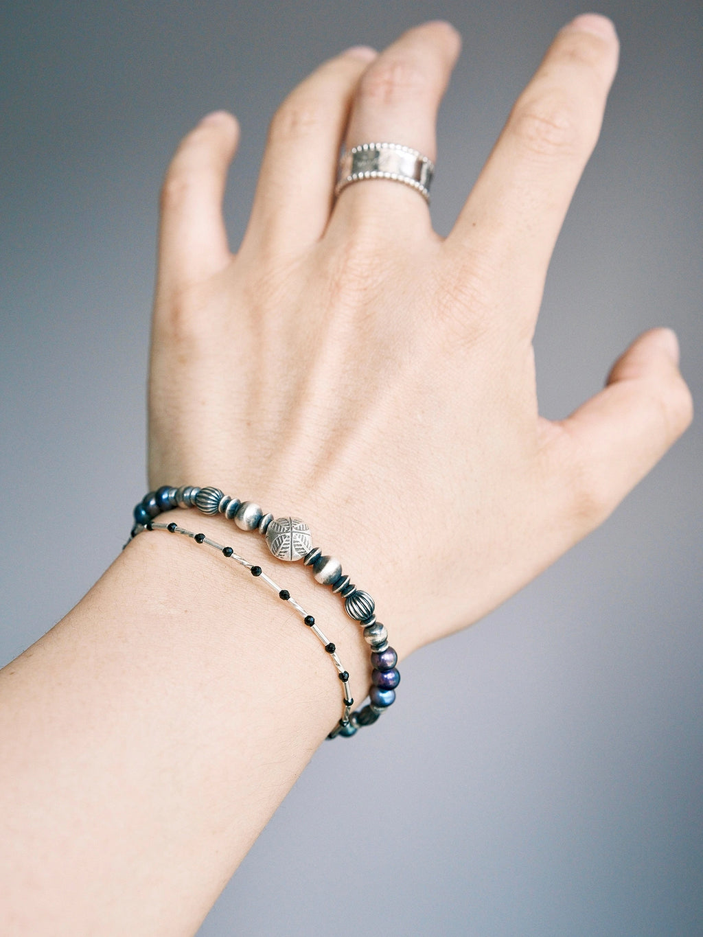 Men wearing a pearl and hammered silver bracelet on wrist, stacked with a slim black beaded bracelet, daily wear masculine style.