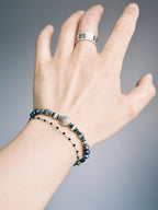 Men wearing a pearl and hammered silver bracelet on wrist, stacked with a slim black beaded bracelet, daily wear masculine style.