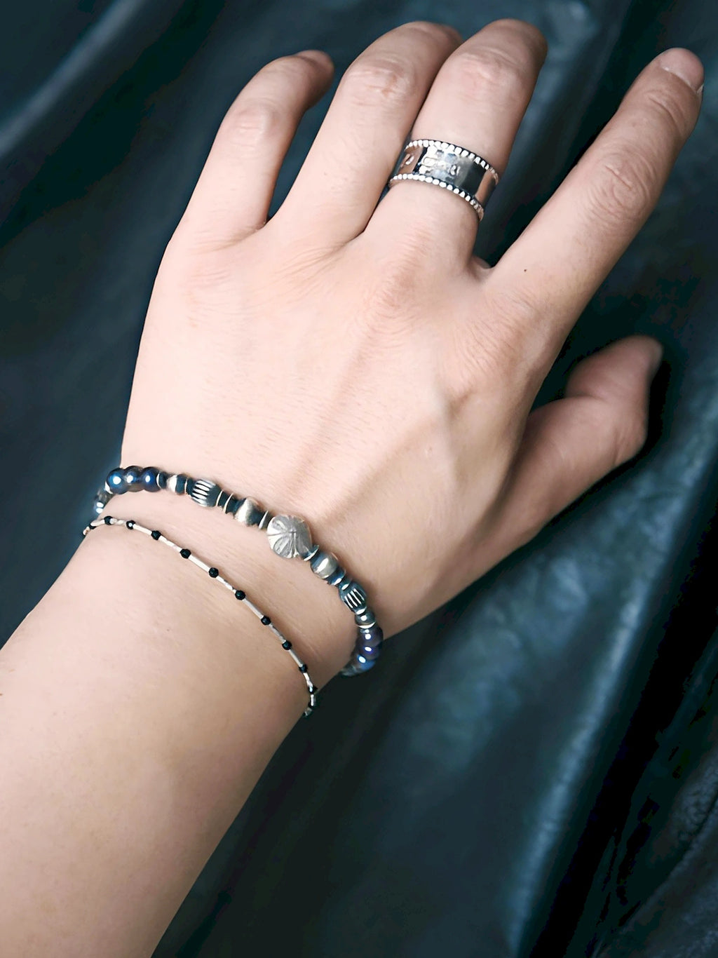 Men’s pearl bracelet stacked with a slim black bracelet, layered wrist styling, quiet luxury masculine jewelry.