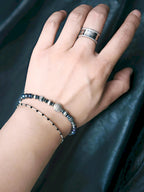 Men’s pearl bracelet stacked with a slim black bracelet, layered wrist styling, quiet luxury masculine jewelry.