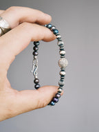 Handheld men’s pearl bracelet with hammered silver beads, close-up product view, Urban Stoic minimal style.