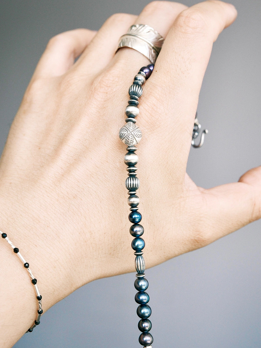 Handheld men’s pearl bracelet with hammered silver beads, close-up product view, Urban Stoic minimal style.