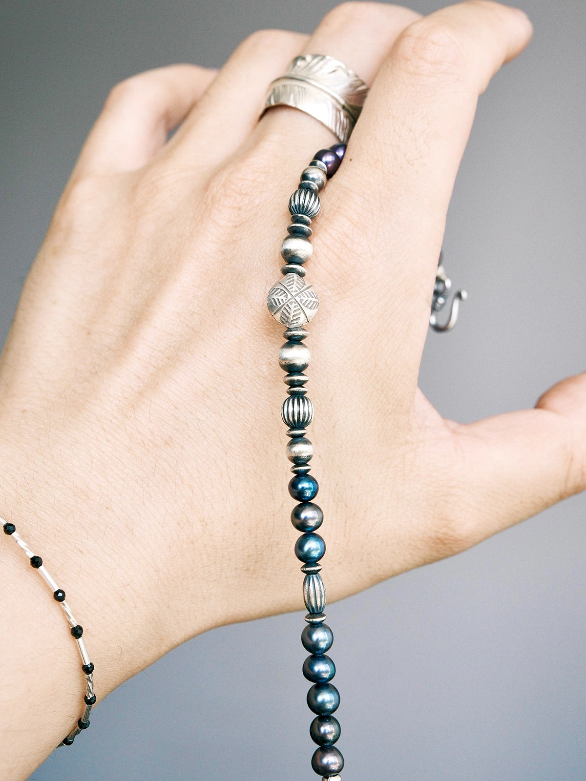 Handheld men’s pearl bracelet with hammered silver beads, close-up product view, Urban Stoic minimal style.