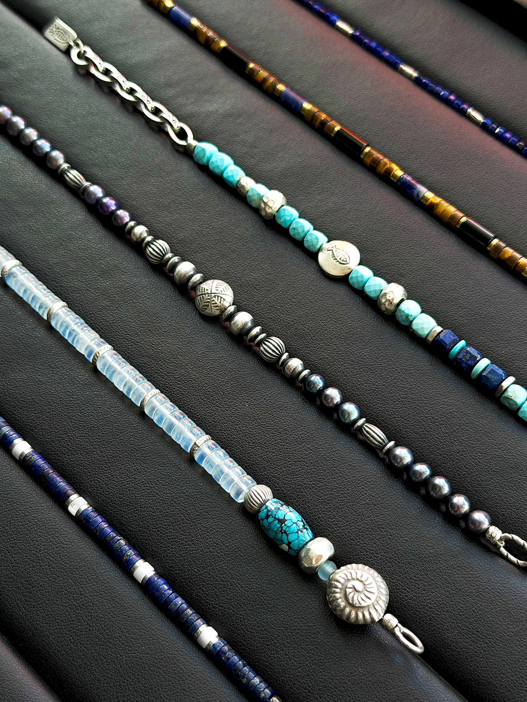 Men’s natural pearl and hammered silver bracelet laid flat on dark wood, cold ocean tones, refined masculine jewelry.