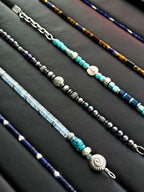 Men’s natural pearl and hammered silver bracelet laid flat on dark wood, cold ocean tones, refined masculine jewelry.