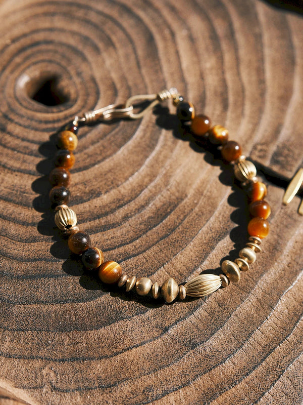 Tiger eye men’s bracelet on rustic wood surface, natural stone beads and refined brass accents with grounded organic texture.