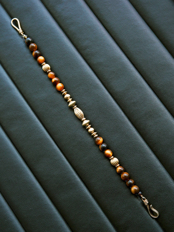 Moody black leather jewelry scene with tiger eye bracelet and refined brass details, masculine Urban Stoic styling for men.