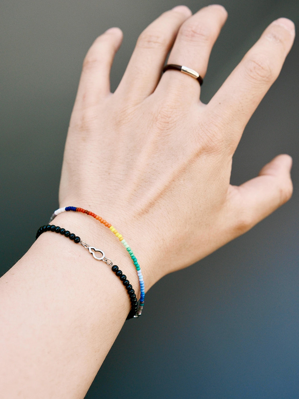 Men’s bracelet stack with thin rainbow colored-glaze bracelet and black bead bracelet, casual wrist styling aesthetic