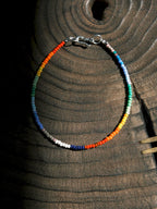 Ultra-thin rainbow colored-glaze men’s bracelet with sterling silver clasp, flat lay on dark textured background, minimal identity style