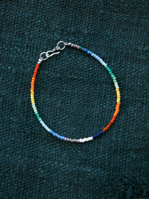 Ultra-thin rainbow colored-glaze men’s bracelet with sterling silver clasp, flat lay on dark textured background, minimal identity style