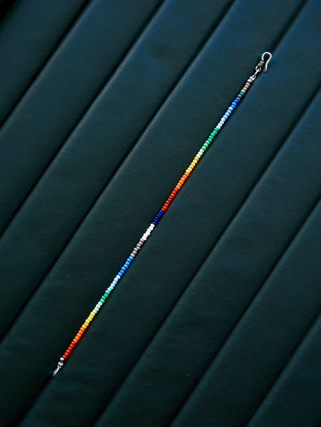Straight layout of thin rainbow colored-glaze bracelet, sterling silver clasp, modern men’s beaded bracelet design