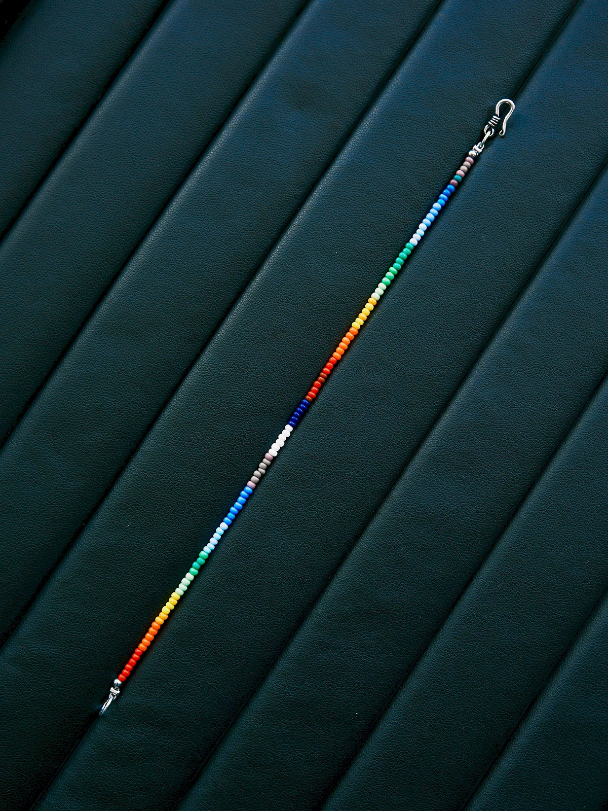 Straight layout of thin rainbow colored-glaze bracelet, sterling silver clasp, modern men’s beaded bracelet design