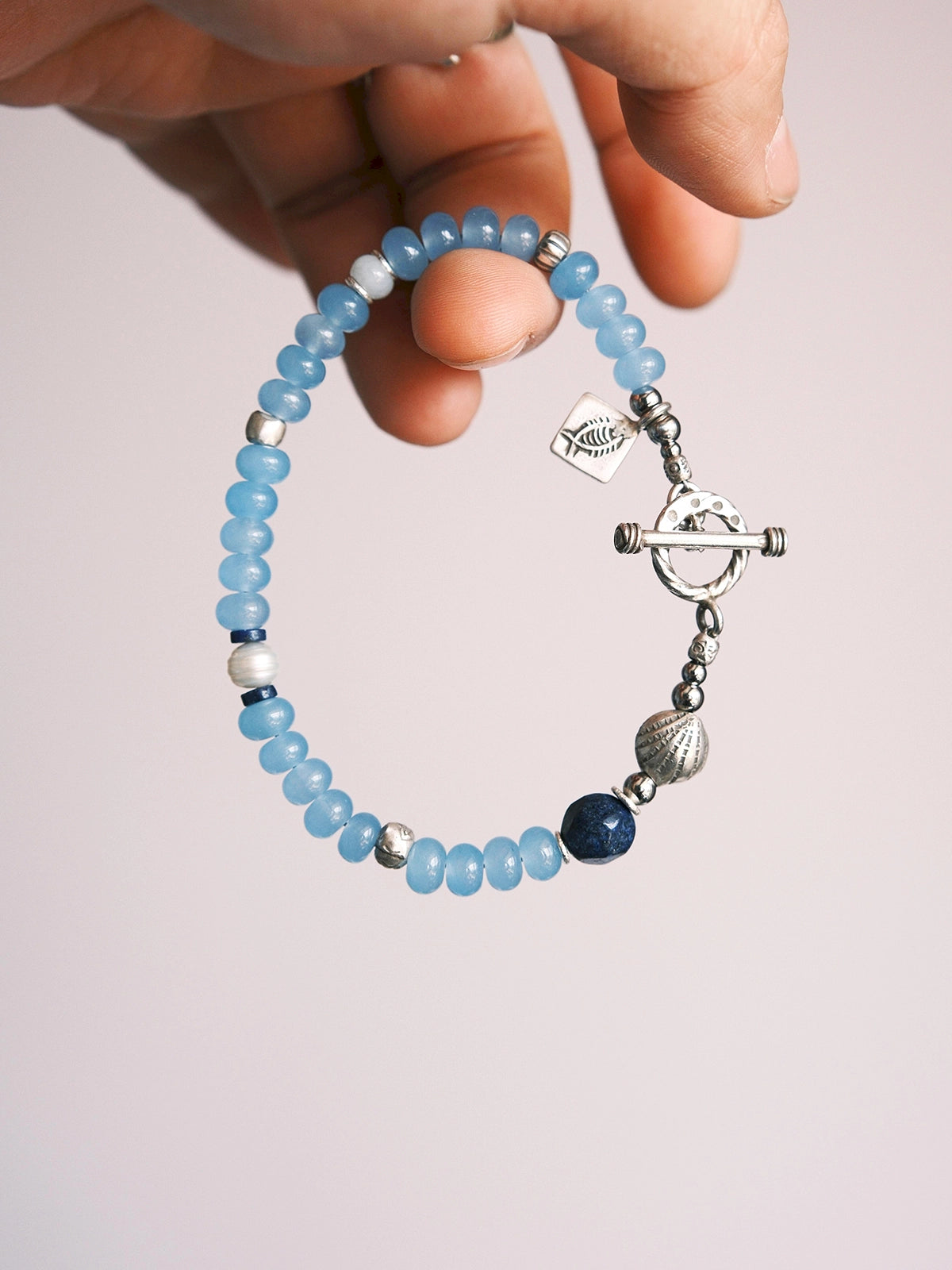 Hand holding Mineral Soul Series Blue Shoal bracelet with blue chalcedony beads, lapis lazuli accent and sterling silver toggle clasp