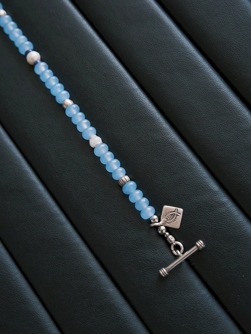 Blue Shoal bracelet on dark textured fabric, cool ocean mood, sterling silver details and refined masculine jewelry aesthetic