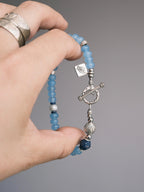 Hand holding Mineral Soul Series Blue Shoal bracelet with blue chalcedony beads, lapis lazuli accent and sterling silver toggle clasp