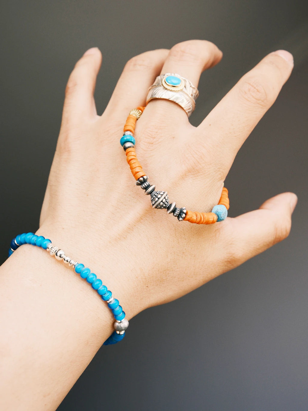 Hand holding a men’s turquoise and sterling silver bracelet, close-up view of sunset orange colored-glaze beads and vintage metal details.