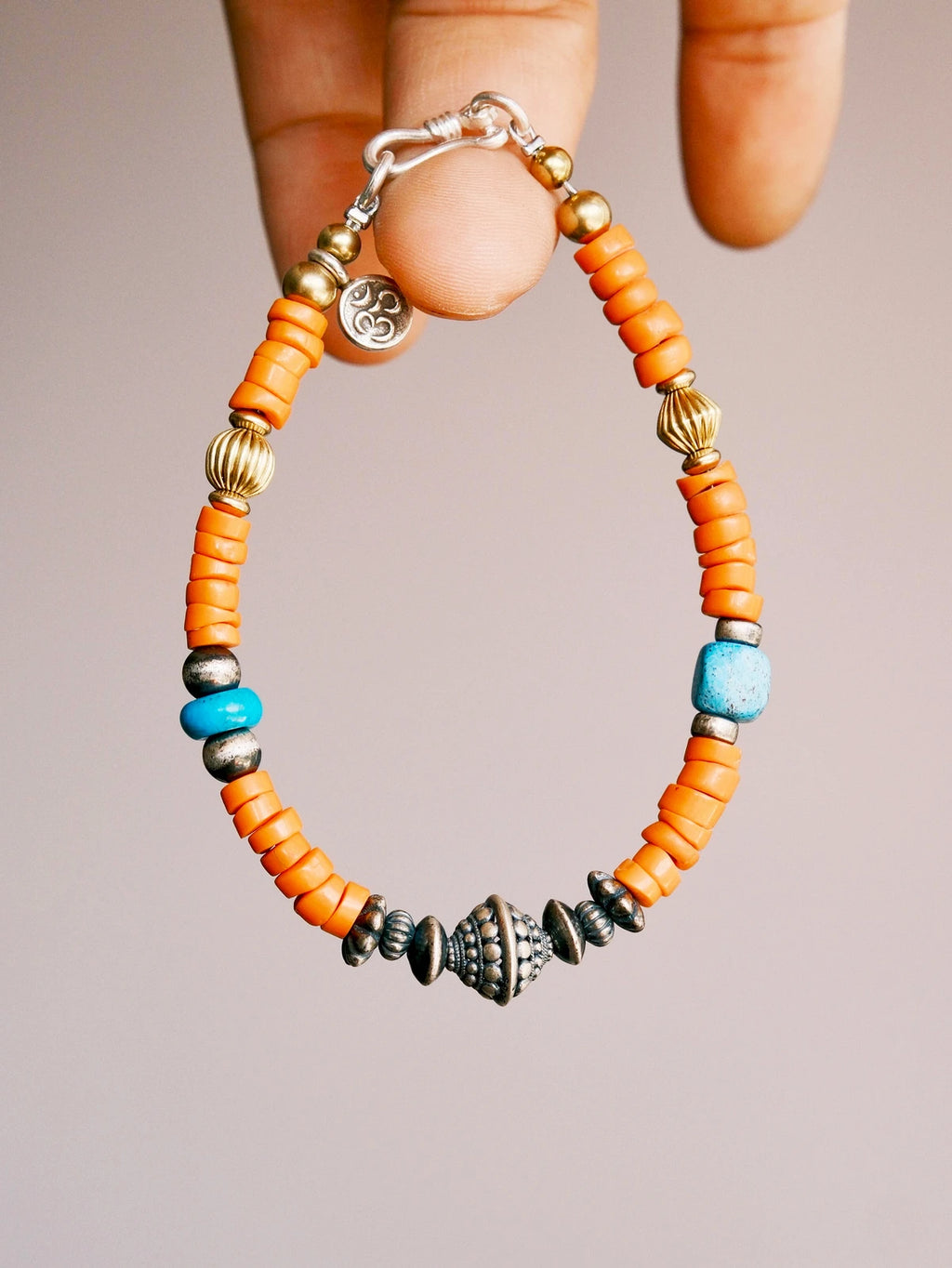 Hand holding a men’s turquoise and sterling silver bracelet, close-up view of sunset orange colored-glaze beads and vintage metal details.