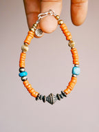 Hand holding a men’s turquoise and sterling silver bracelet, close-up view of sunset orange colored-glaze beads and vintage metal details.