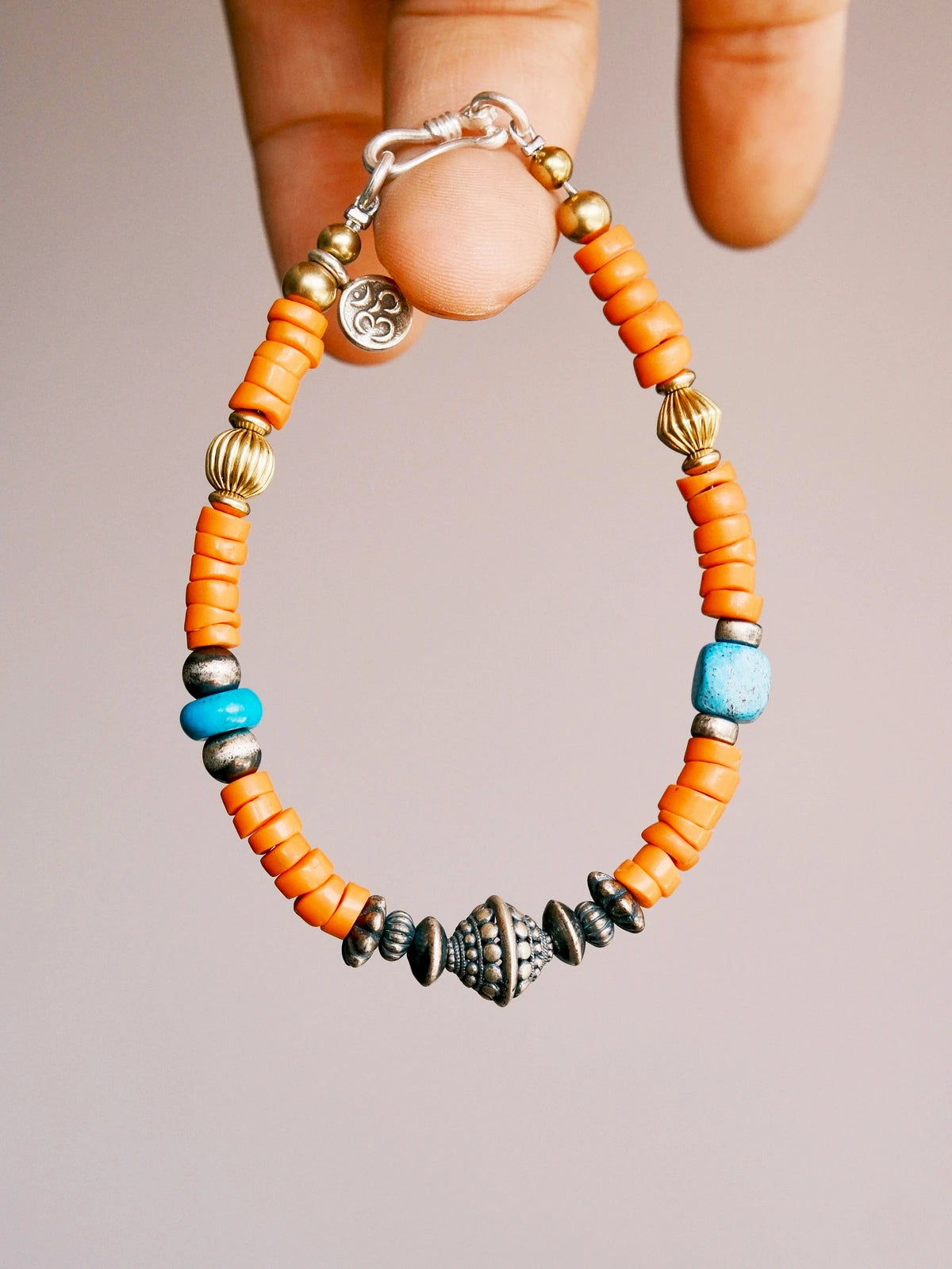 Hand holding a men’s turquoise and sterling silver bracelet, close-up view of sunset orange colored-glaze beads and vintage metal details.