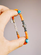 Hand holding a men’s turquoise and sterling silver bracelet, close-up view of sunset orange colored-glaze beads and vintage metal details.