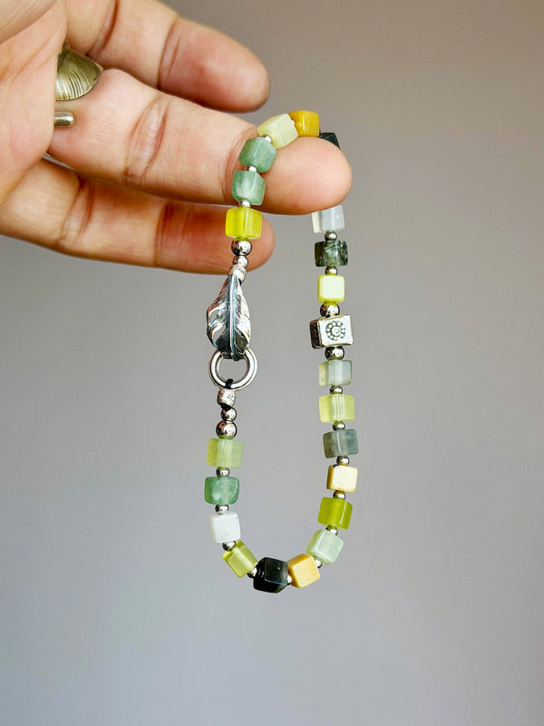 Hand holding men’s Xiuyu jade beaded bracelet with 925 silver feather, natural stone texture close-up