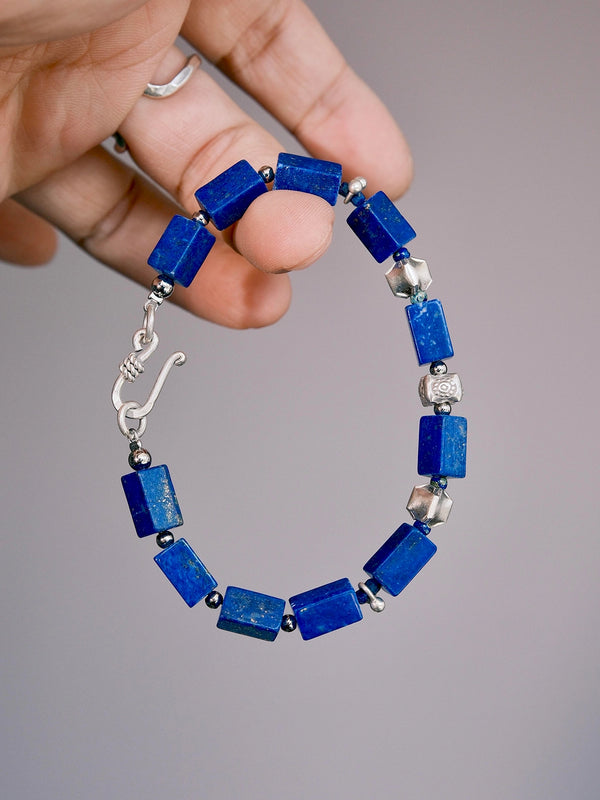 Hand holding a rectangular lapis lazuli bracelet with hammered 990 fine silver details and a silver hook clasp.