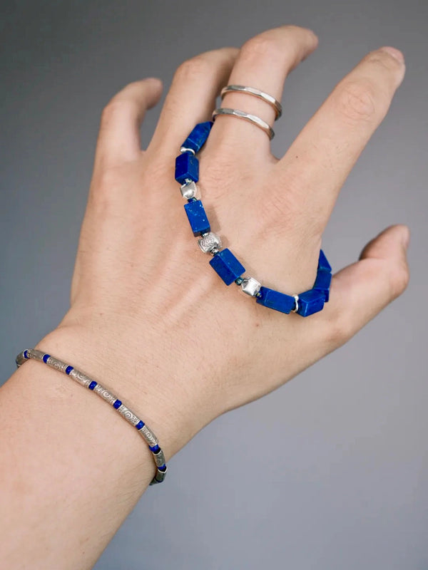 Hand holding a rectangular lapis lazuli bracelet with hammered 990 fine silver details and a silver hook clasp.