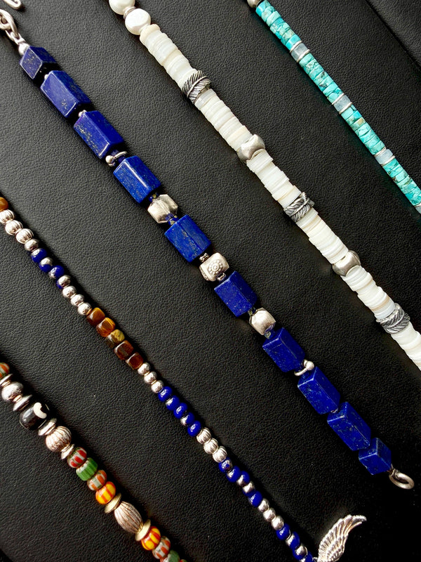 Blue lapis lazuli and silver bracelet displayed with other gemstone designs in an artistic men’s jewelry collection.