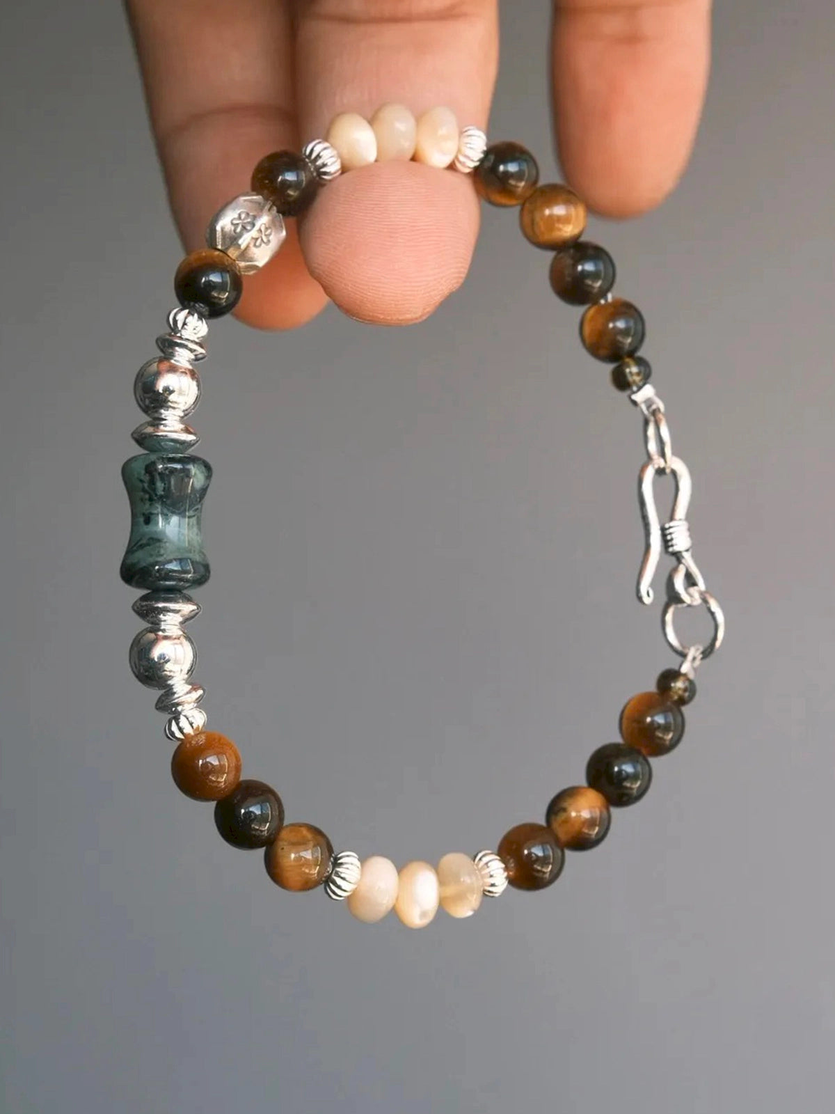 Hand-held Ochre Monarch men’s bracelet with tiger eye, mother-of-pearl, agate and 925 sterling silver against a gray background
