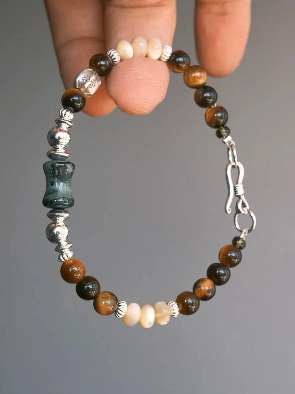 Hand-held Ochre Monarch men’s bracelet with tiger eye, mother-of-pearl, agate and 925 sterling silver against a gray background