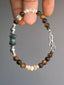 Hand-held Ochre Monarch men’s bracelet with tiger eye, mother-of-pearl, agate and 925 sterling silver against a gray background