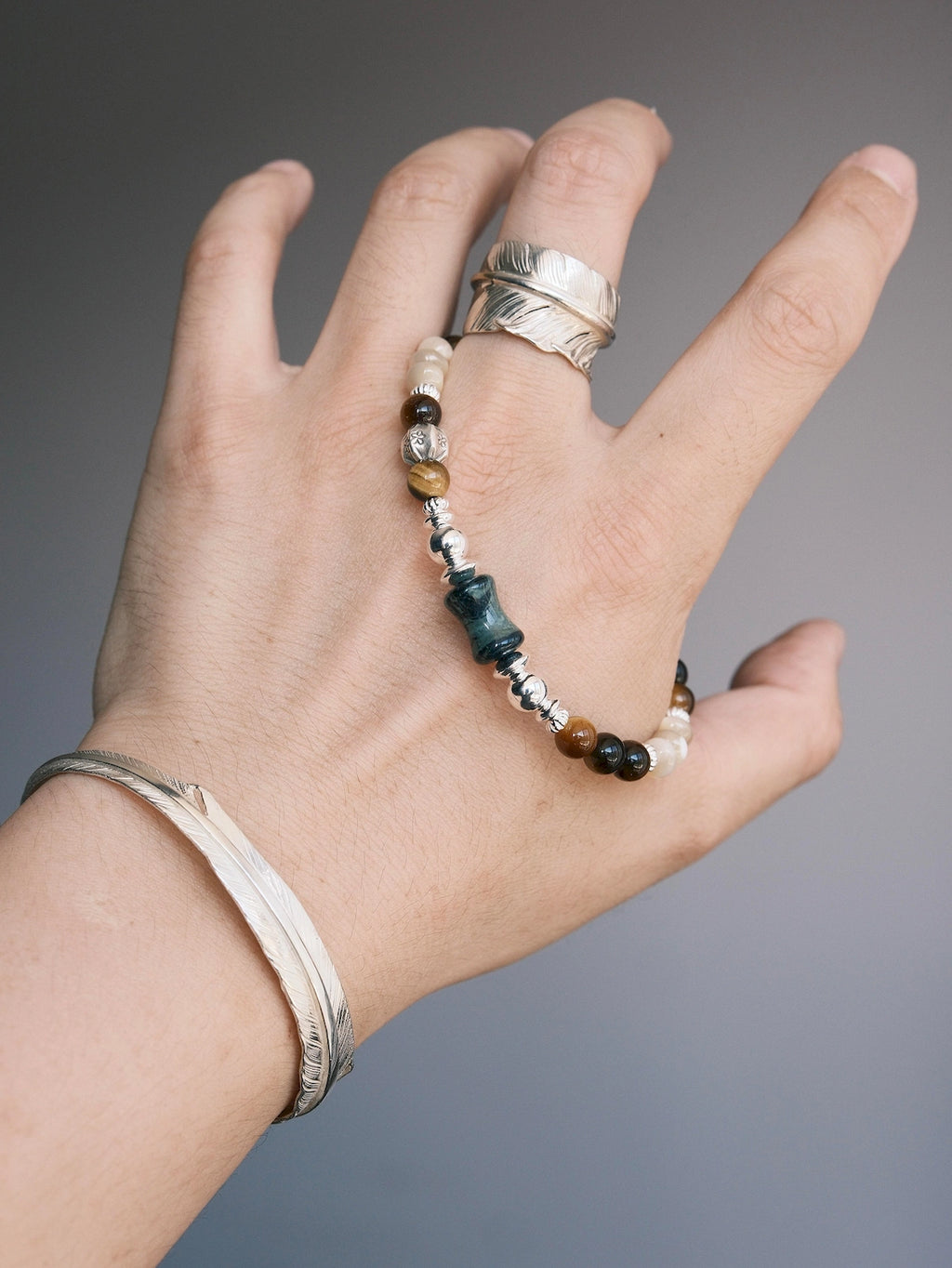 Ochre Monarch gemstone bracelet draped across a hand with a silver feather ring and cuff, highlighting its earthy color palette