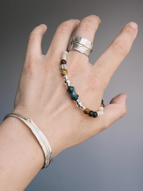 Ochre Monarch gemstone bracelet draped across a hand with a silver feather ring and cuff, highlighting its earthy color palette