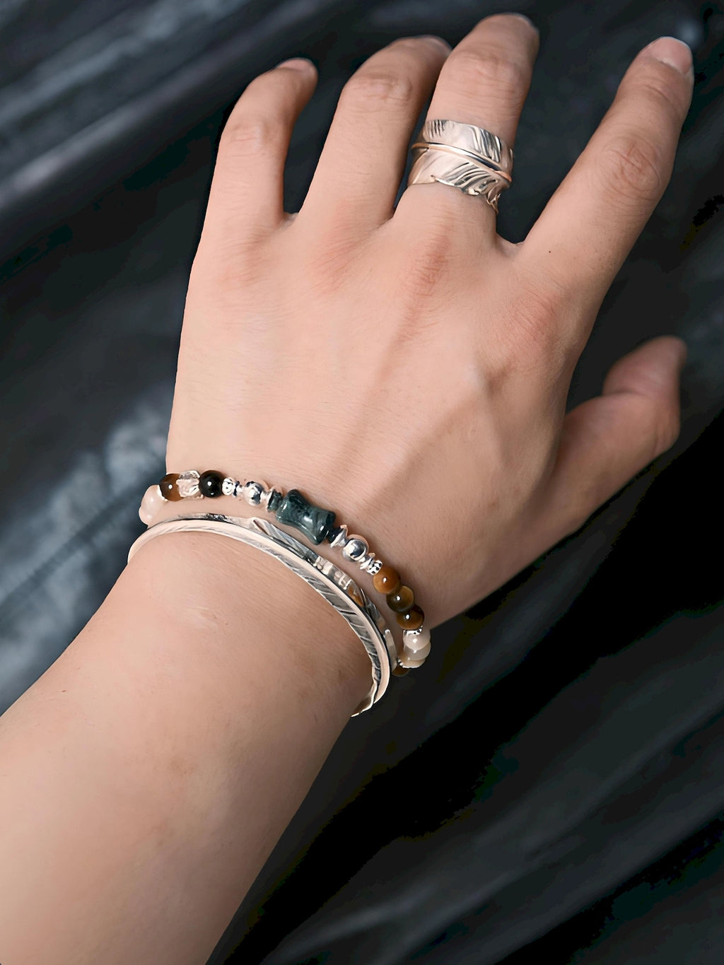 Close wrist view of the Ochre Monarch gemstone bracelet stacked with a silver cuff against a dark leather background