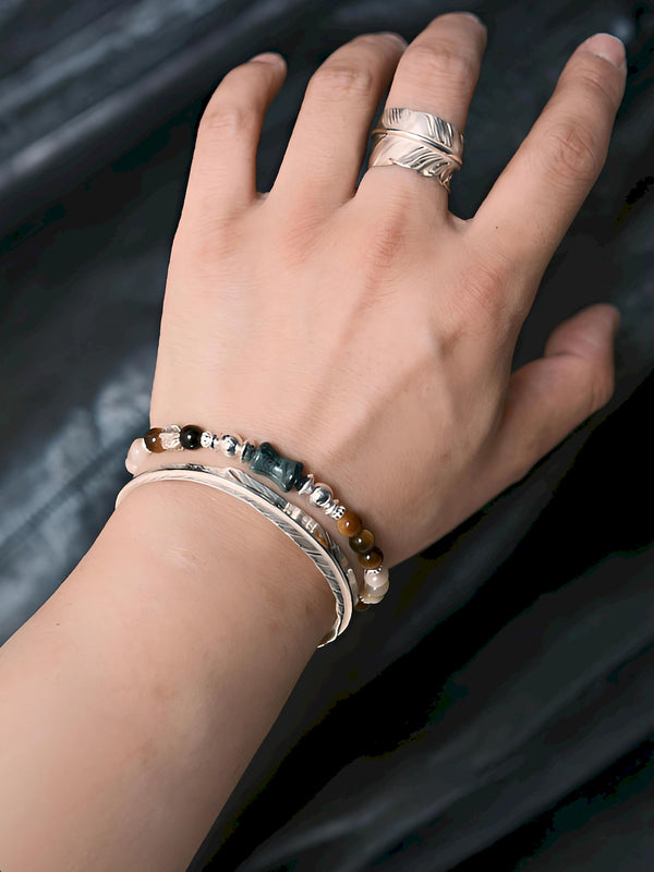 Close wrist view of the Ochre Monarch gemstone bracelet stacked with a silver cuff against a dark leather background
