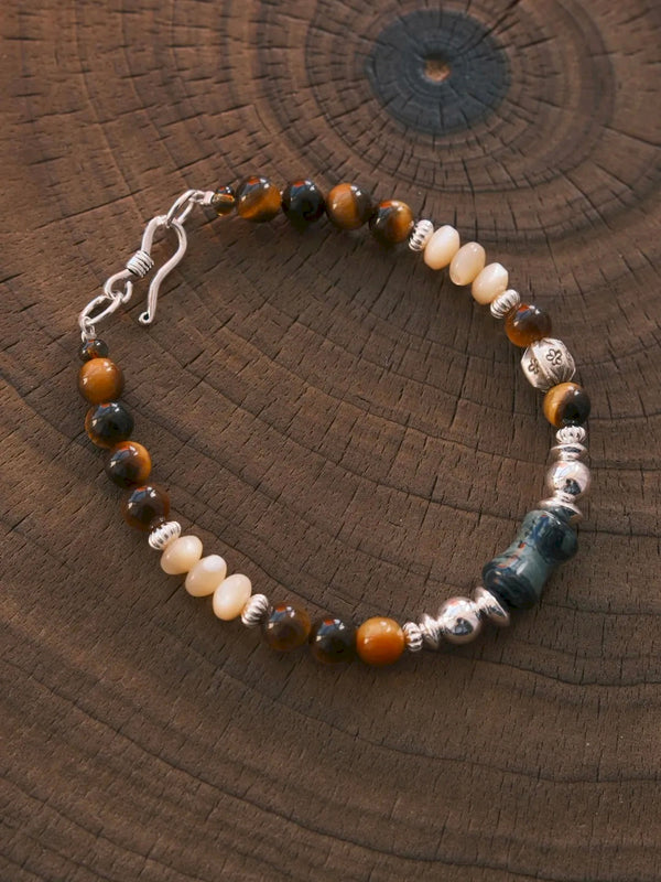 Ochre Monarch tiger eye, mother-of-pearl and sterling silver bracelet arranged on a natural wood-grain surface