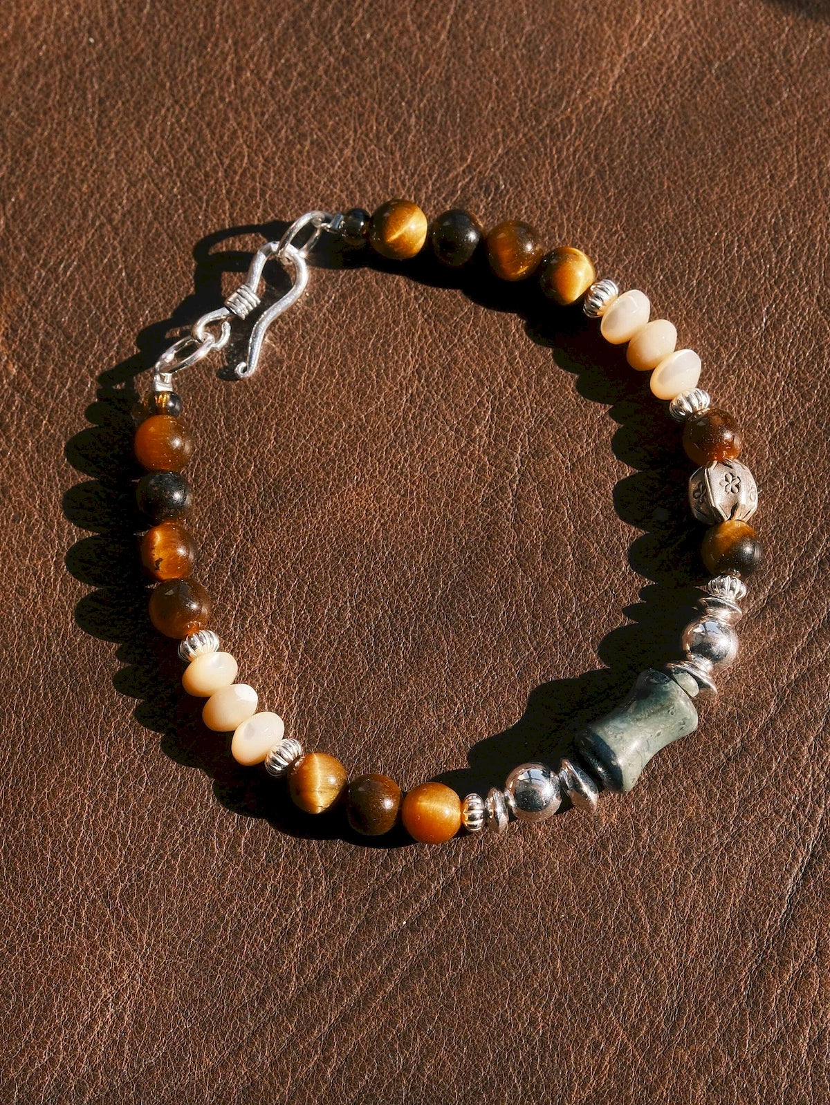 Sunlit flat lay of the Ochre Monarch men’s bracelet with tiger eye, agate, mother-of-pearl and sterling silver on brown leather