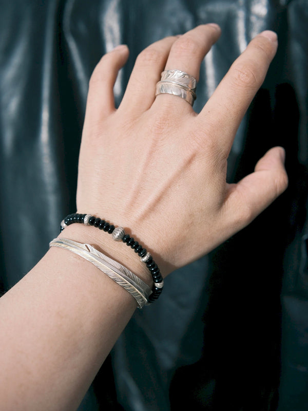 Black onyx and hammered silver bracelet stacked with slim silver cuffs on a man's wrist