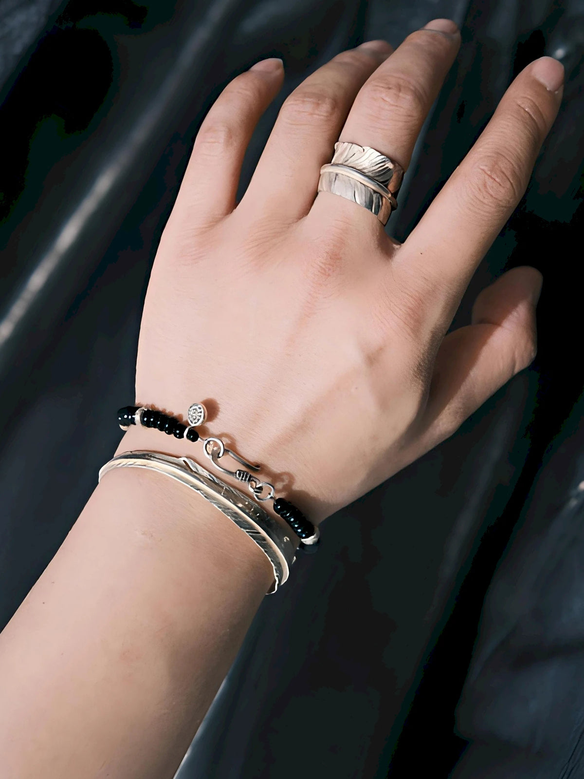 Black onyx and hammered silver bracelet stacked with slim silver cuffs on a man's wrist