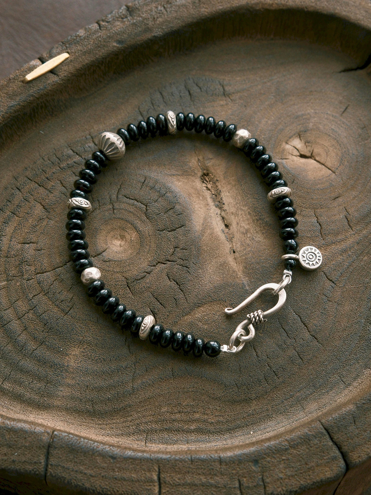 Dawn Sentinel black onyx bracelet with hammered silver beads and an fishhook clasp in a wooden flat lay