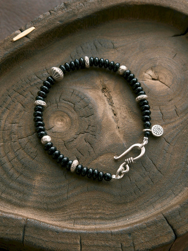 Dawn Sentinel black onyx bracelet with hammered silver beads and an fishhook clasp in a wooden flat lay