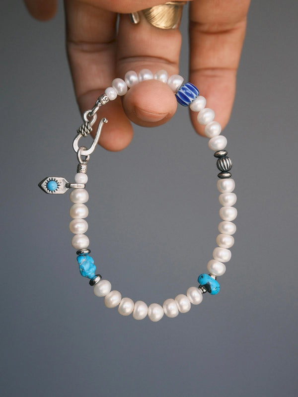 Pearl Rebel held in one hand, with white pearls, turquoise accents and a blue striped bead