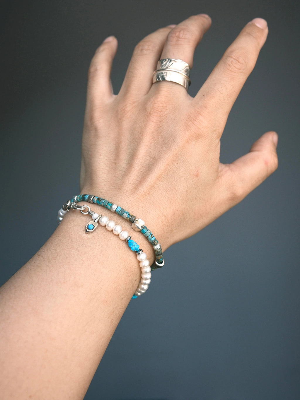 Pearl Rebel on the wrist beside a turquoise bracelet, with its small charm and clasp visible